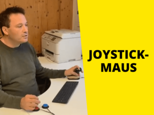 Mann sitzt am Schreibtisch und bedient einen Joystick und zwei Knöpfe, rechts Text auf gelb "Joystick Maus"