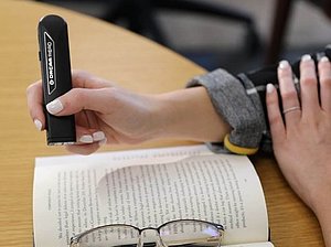 Person bedient schwarzes Gerät, das aussieht wie Laserpointer über einem Buch