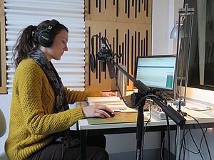 Eine Frau sitzt in einem Tonstudio und liest einem Mikrofon ein Buch vor