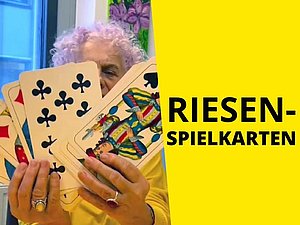 Frau hält Schnapskarten in Übergröße hoch um sie zu zeigen. Text: "Riesenspielkarten"