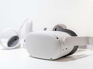Weiße VR Brille liegt auf einem weißen Untergrund, Zubehör verschwommen im Hintergrund.