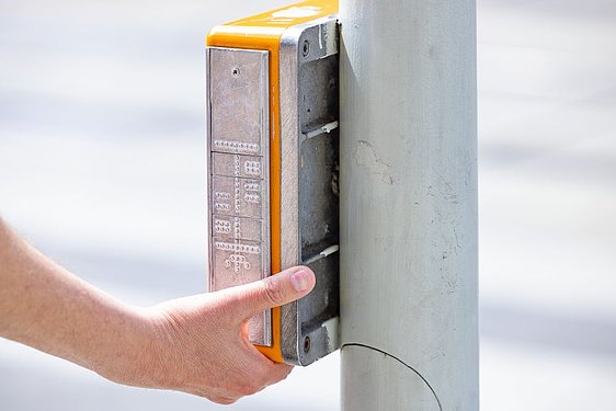 Hand drückt Akustische Ampel mit taktiler Topografie der Kreuzung drauf