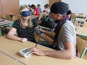 Schüler misst Blutdruck bei einer Schülerin mit Augenbinde