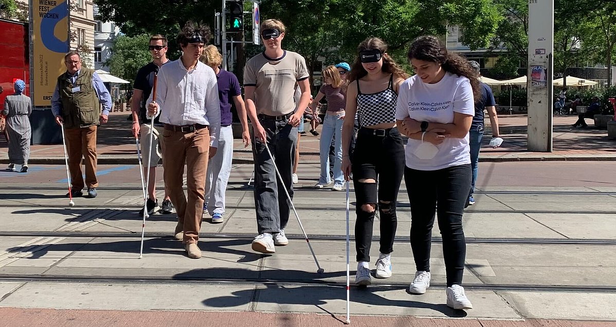 Einige Menschen gehen auf einem Zebrastreifen mit weißen Stöcken und Augenbinden.