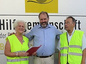 Hubert Wagner posiert mit „Ampelpaten“ Veronika Kerschbaum und Michael Watz lächelnd für ein Foto vor dem Eingang der Hilfsgemeinschaft.