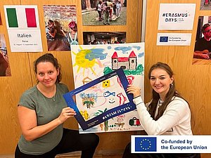 Eröffnung der Fotoausstellung Zwei junge Frauen halten einen Bilderrahmen, im Hintergrund sieht man Fotos