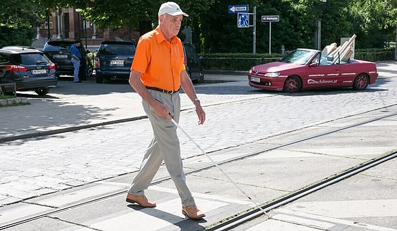 Blinder Mann geht mit einem Taststock über einen Zebrastreifen.