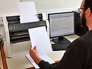 Mann von hinten schaut sich Brailledruck an vor einem Drucker