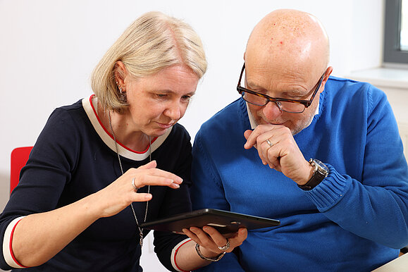 Ein Mann und eine Frau sitzen über ein Tablet gebeugt da.