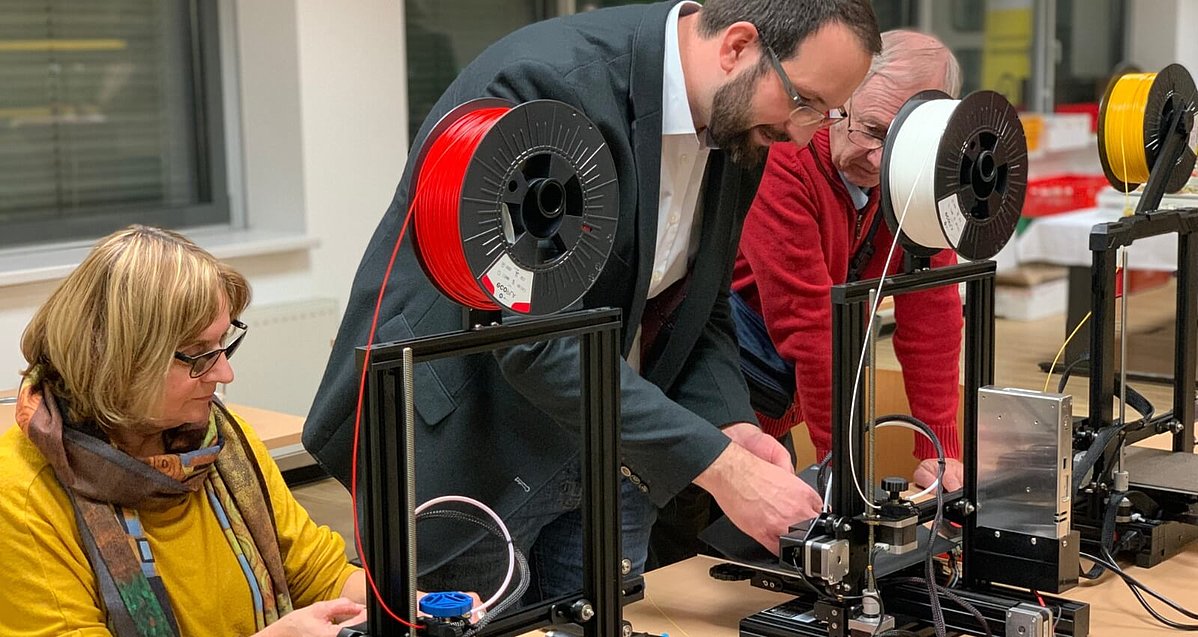 Zwei Männer nehmen eine Einstellung an einem von mehreren 3D Druckern vor.