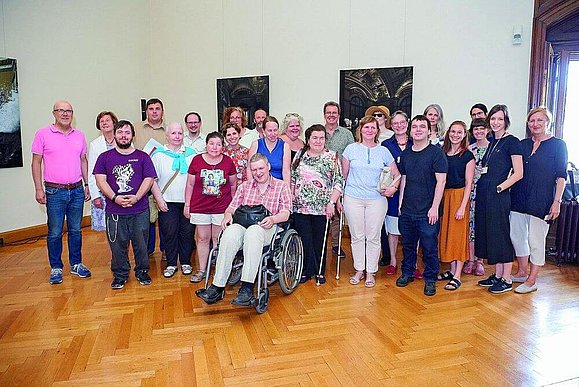 Die Teilnehmerinnen und Teilnehmer von ARCHES, ein Lieblingsprojekt der engagierten Kunstvermittlerin. Gruppenbild von ca 25 Menschen, einige mit Rollstuhl und einige mit Langstock