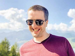 lachender Mann mit Sonnenbrille und purpur Shirt vor blauem Himmel