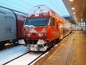 Roter Zug der ÖBB mit Schnee bedeckt, steht am Bahnhof. 