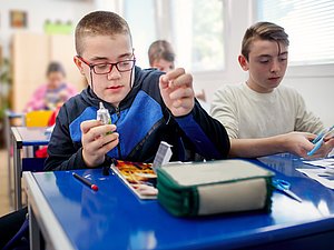 Inklusives Lernen Bub mit Behinderung bastelt in der Schule mit anderen Kindern.