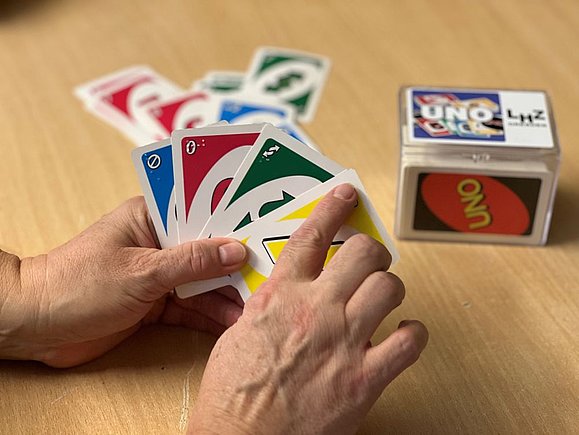 Hand hält Unokarten und berührt Braille in linker Ecke einer Karte