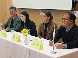 Podium mit zwei Frauen und zwei Männern, die bei einem langen Tisch sitzen. 