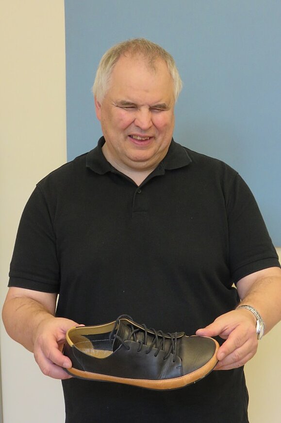 Bruno Kühne hält lächelnd einen grauen Barfußschuh in beiden Händen.