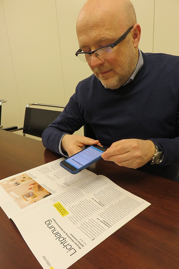 Mitarbeiter Daniele Marano fotografiert mit seinem Smartphone das Magazin Sichtweisen.